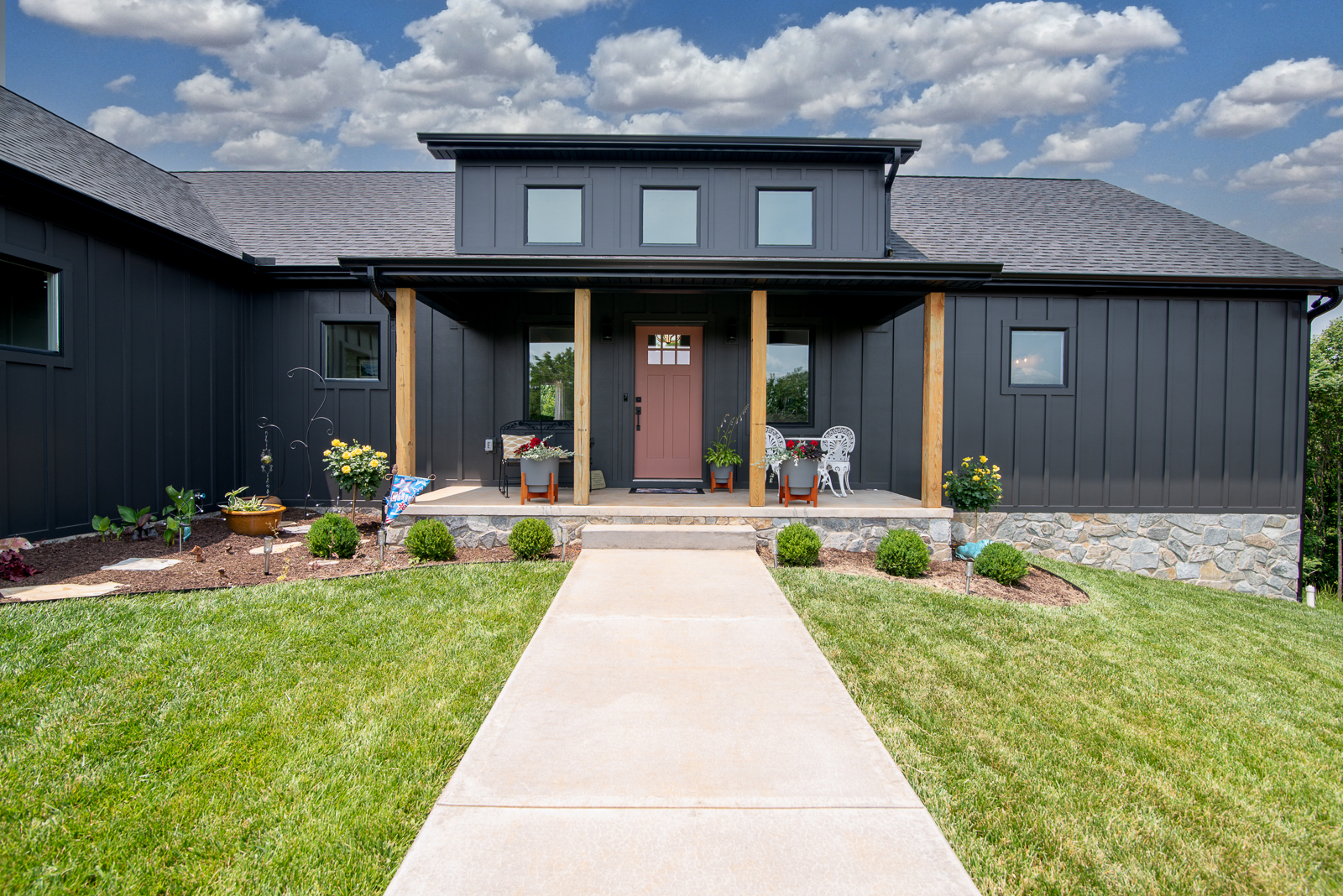 Exterior view of a modern home. This home features black board and batten siding, a statement door, and a natural stone foundation.