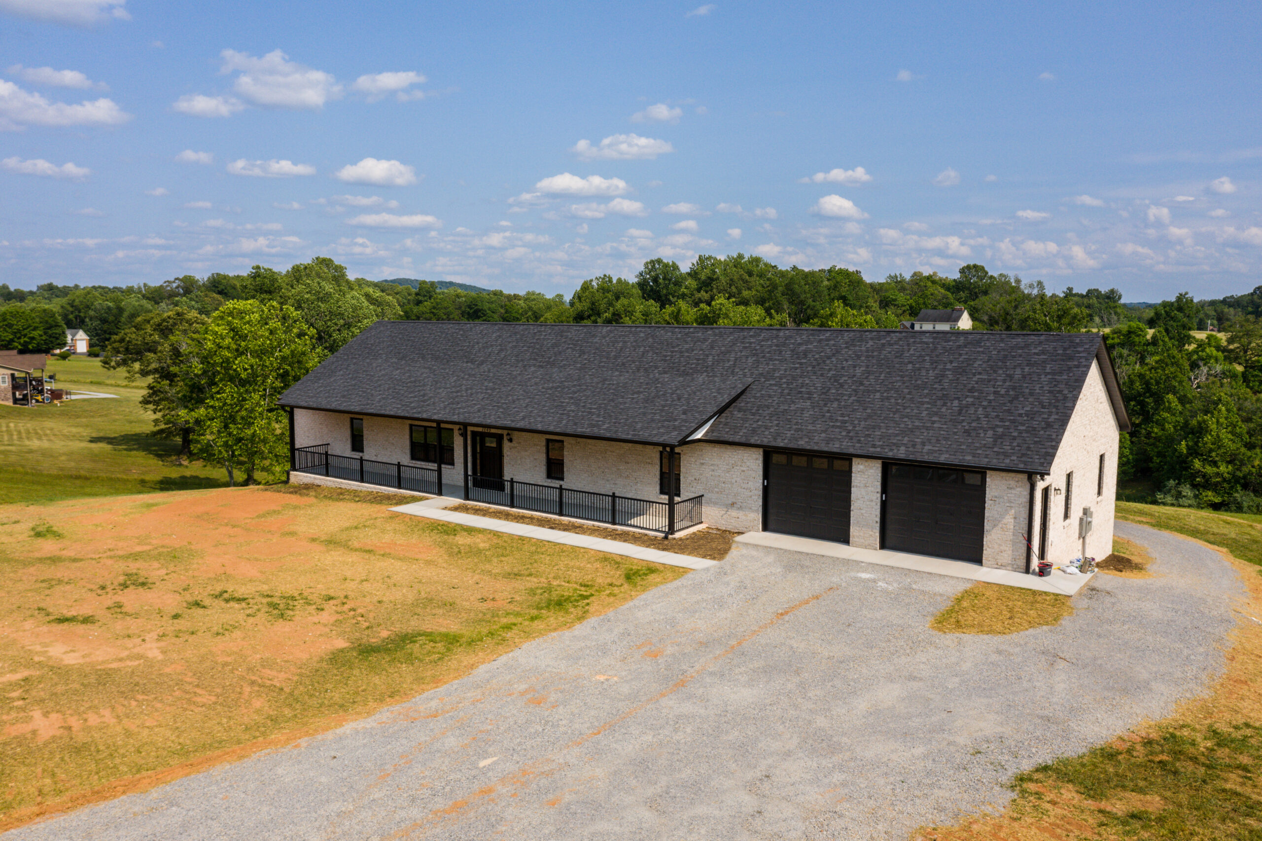 Spacious white brink rancher home with a black shingle roof, black windows and black gutters.