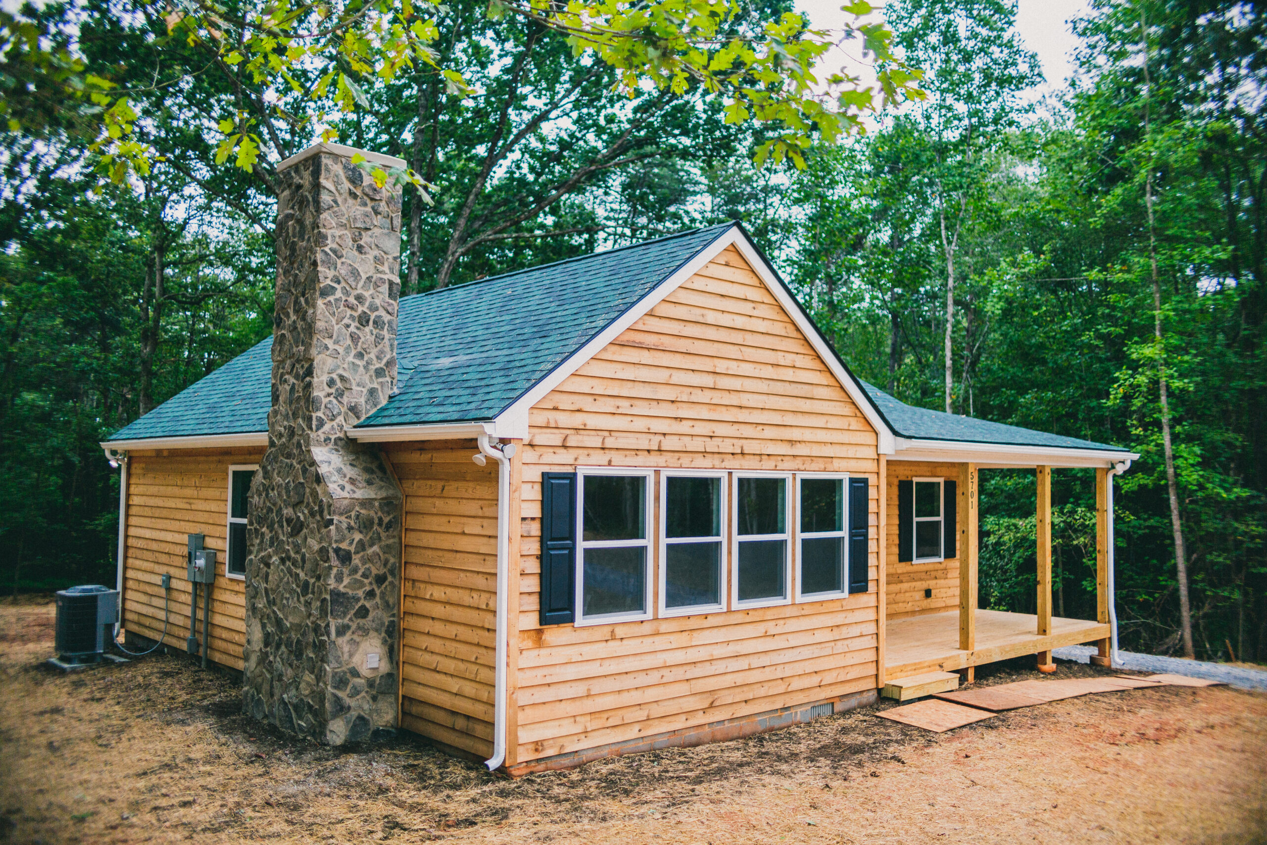Small wood cabin style home with natural stone chimney and front porch.